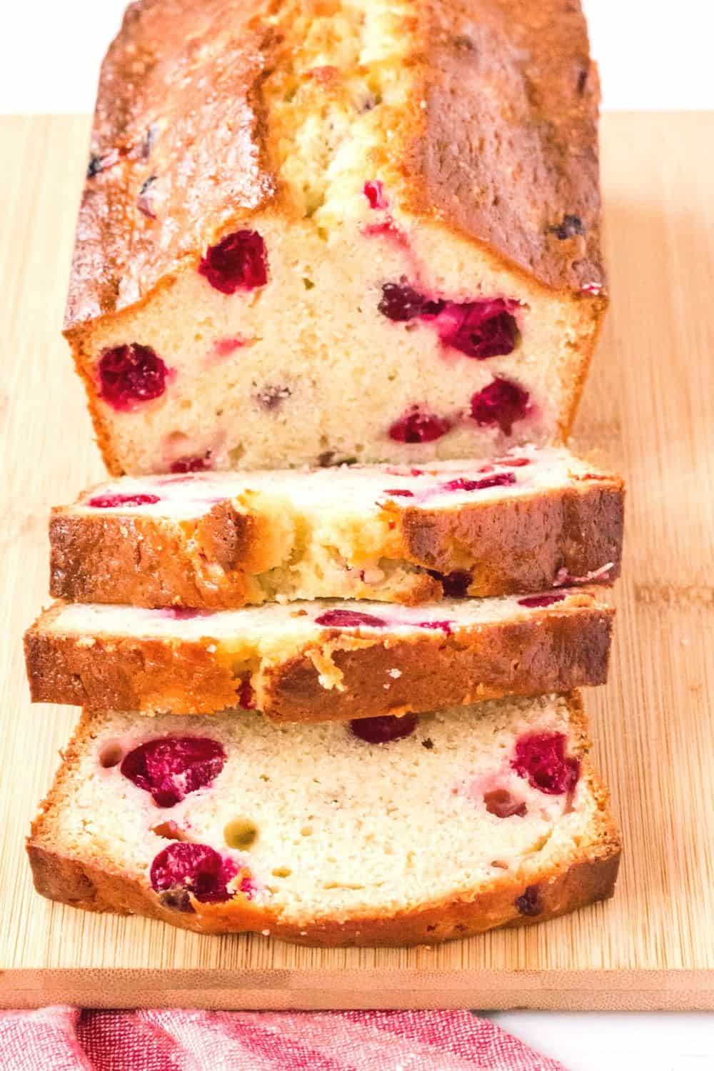 sliced loaf of banana bread with cranberries on a wooden cutting board