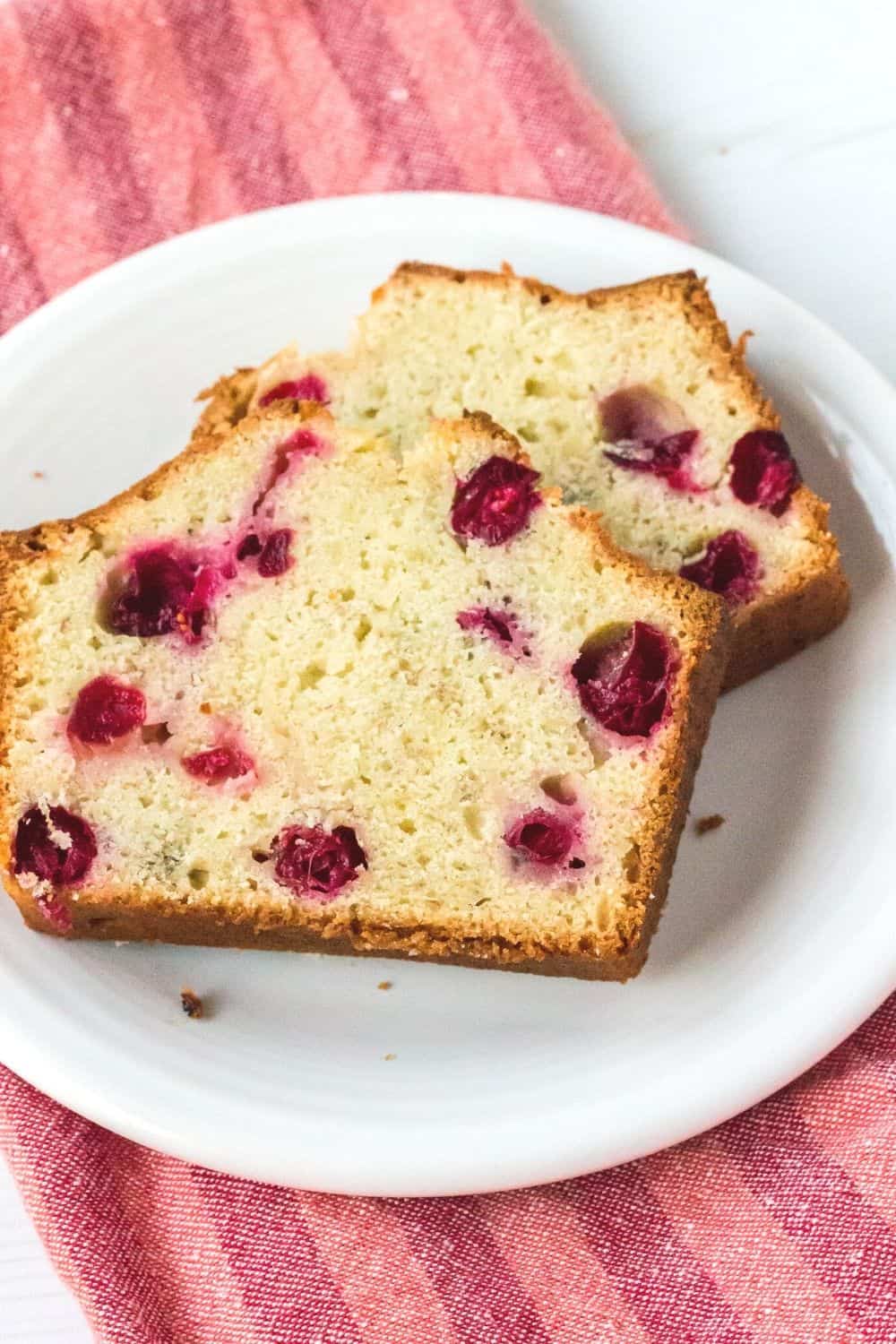slices of banana bread baked with fresh cranberries in the batter served on a white plate atop a red striped napkin