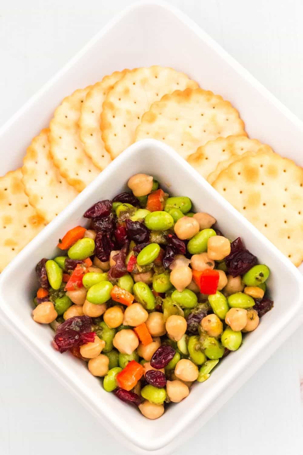 a small white bowl of chickpea salad served on a white plate with several crackers for dipping