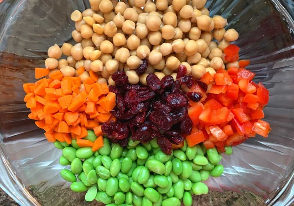 chickpeas, carrots, edamame, cranberries, and bell peppers in a glass mixing bowl