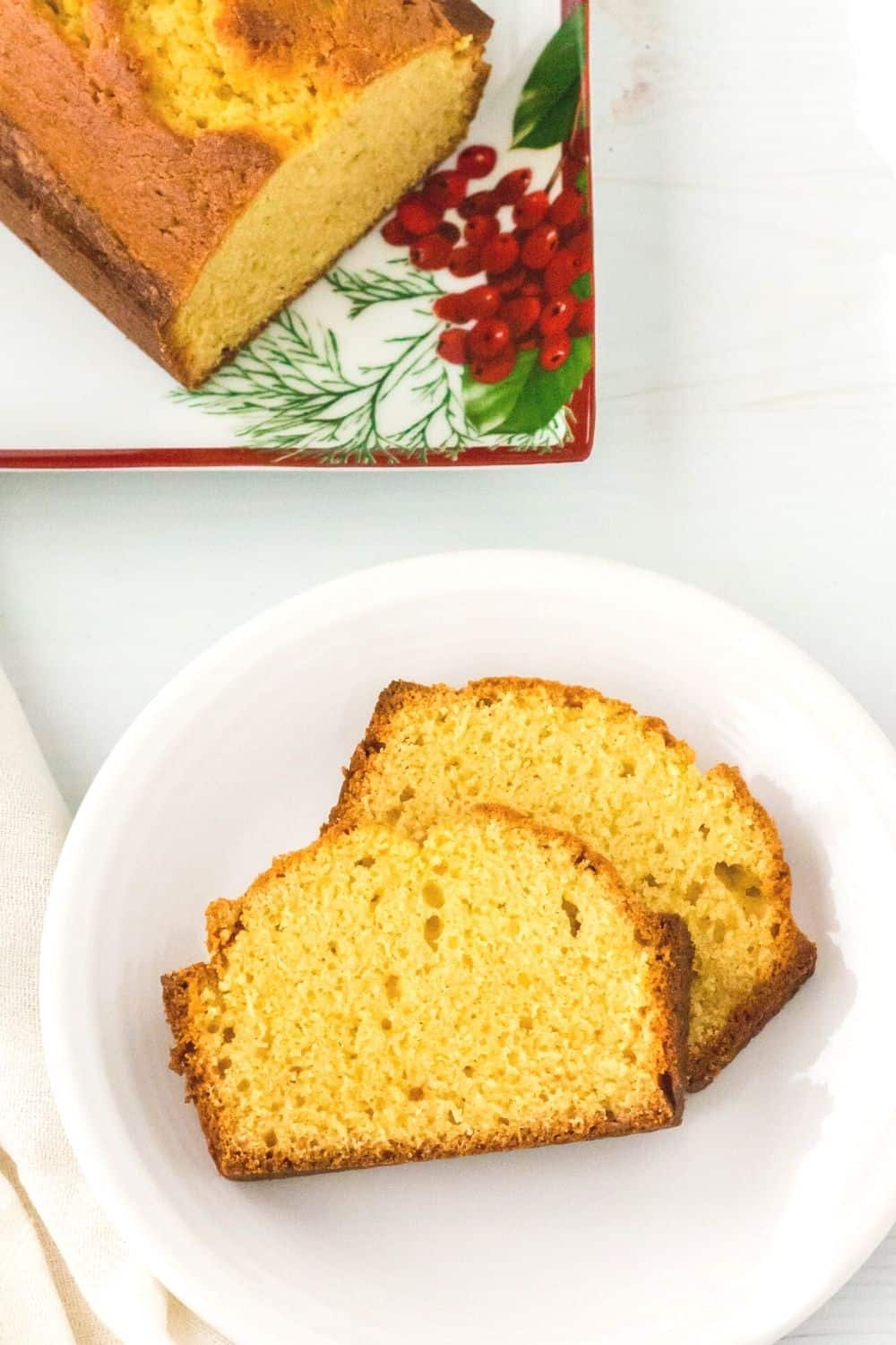 two slices of eggnog bread on a white plate, with the serving plate in the background