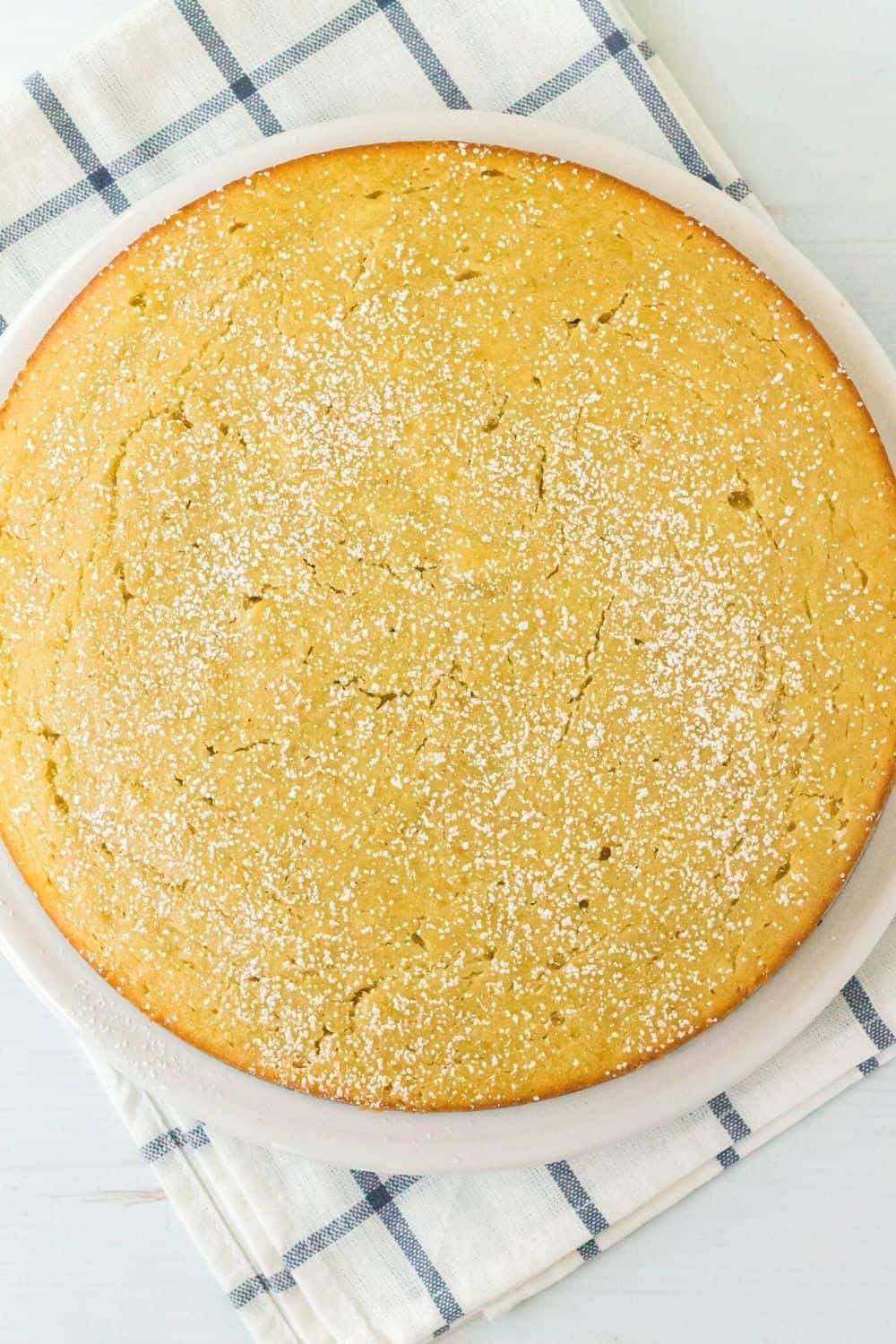 whole pear cake dusted with powdered sugar on a white plate, resting on a blue and white napkin