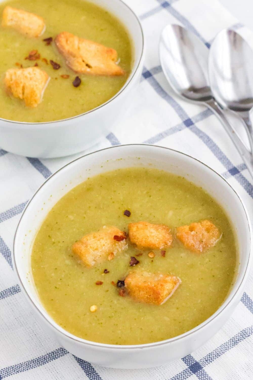 two white bowls of Instant Pot vegan broccoli soup topped with croutons and crushed red pepper flakes