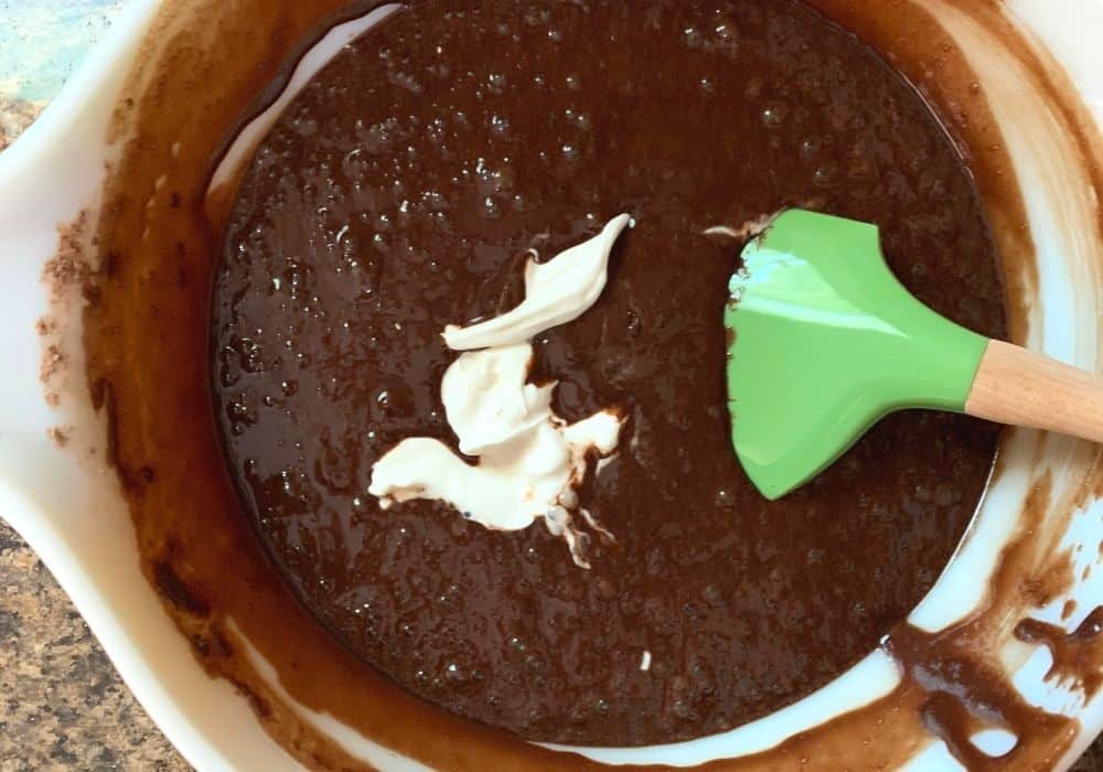 sour cream added to chocolate cake batter in a mixing bowl