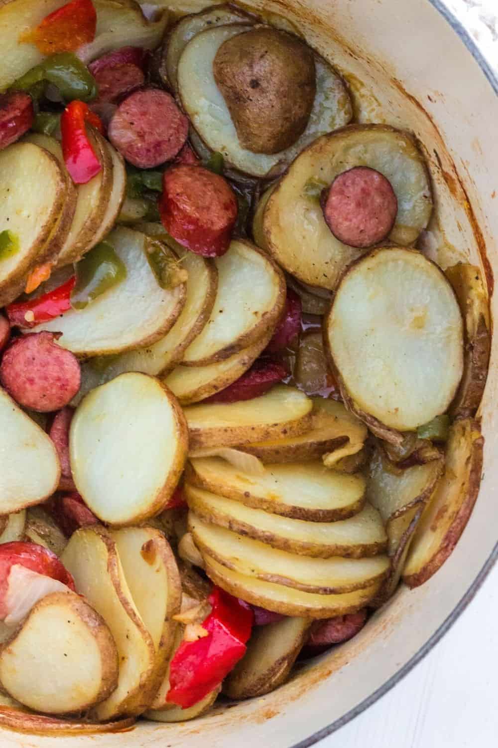 overhead view of a dutch oven filled with smothered potatoes, sausage, onions, and peppers