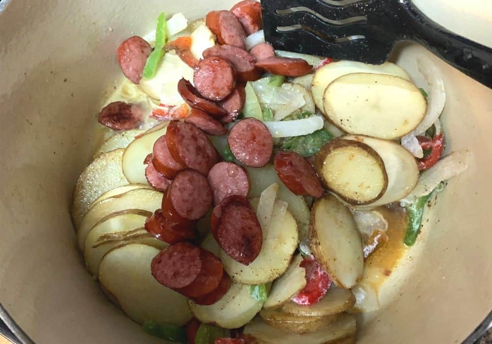 smoked sausage, onions, peppers, potatoes, chicken broth, and seasonings combined in a dutch oven and ready to be baked