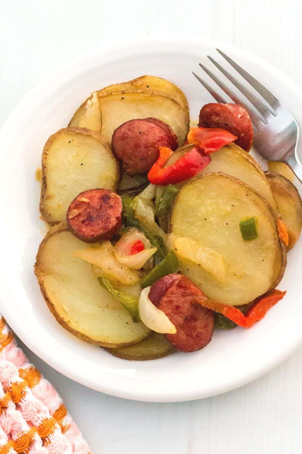 a white plate with a serving of smoked sausage, potatoes, peppers, and onions.