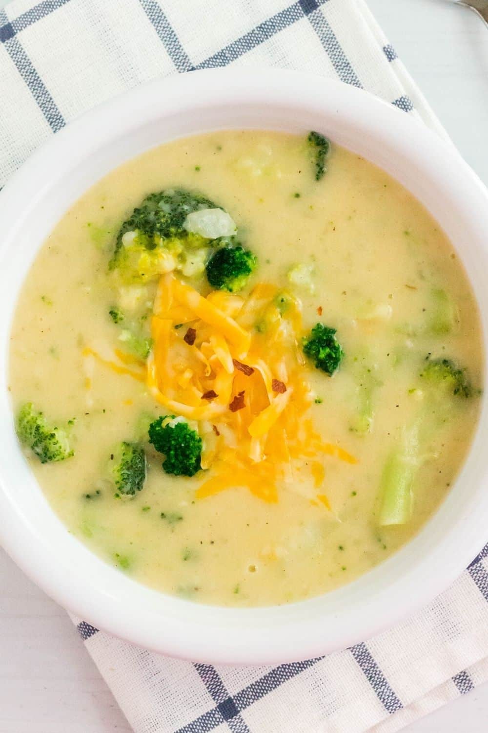 overhead view of a white bowl serving Instant Pot broccoli and potato soup, garnished with shredded cheese