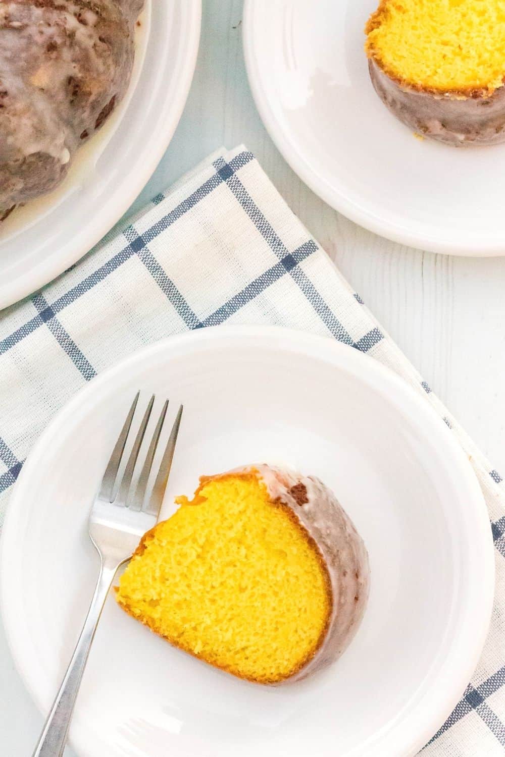aerial view of a slice of cake mix lemon cake on a white plate, with another slice and the remaining cake in the background.
