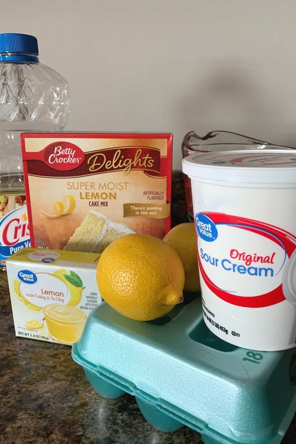 ingredients for the lemon cake, including a lemon cake mix, lemon pudding mix, vegetable oil, fresh lemons, eggs, and sour cream.