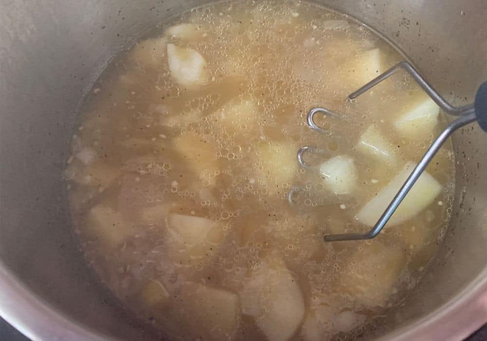 a potato masher is mashing the cooked potatoes in broth