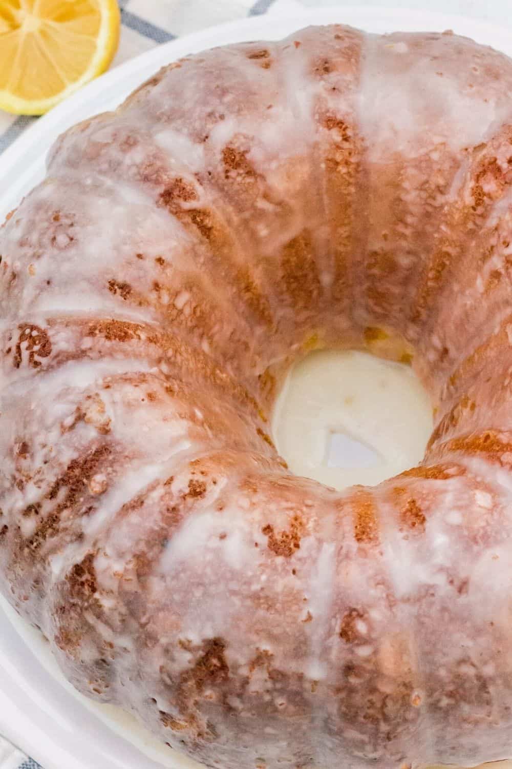 glazed lemon bundt cake with a cut lemon in the background. The glaze has hardened into a satiny finish.