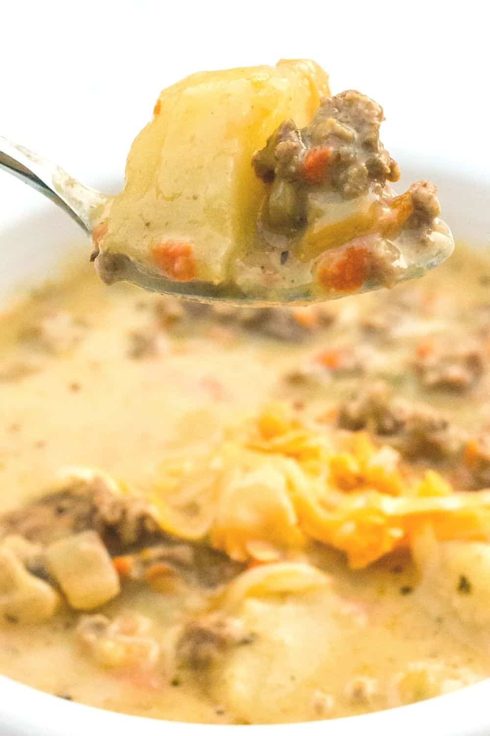 a spoon lifts out a bite of pressure cooker cheeseburger soup from a bowl