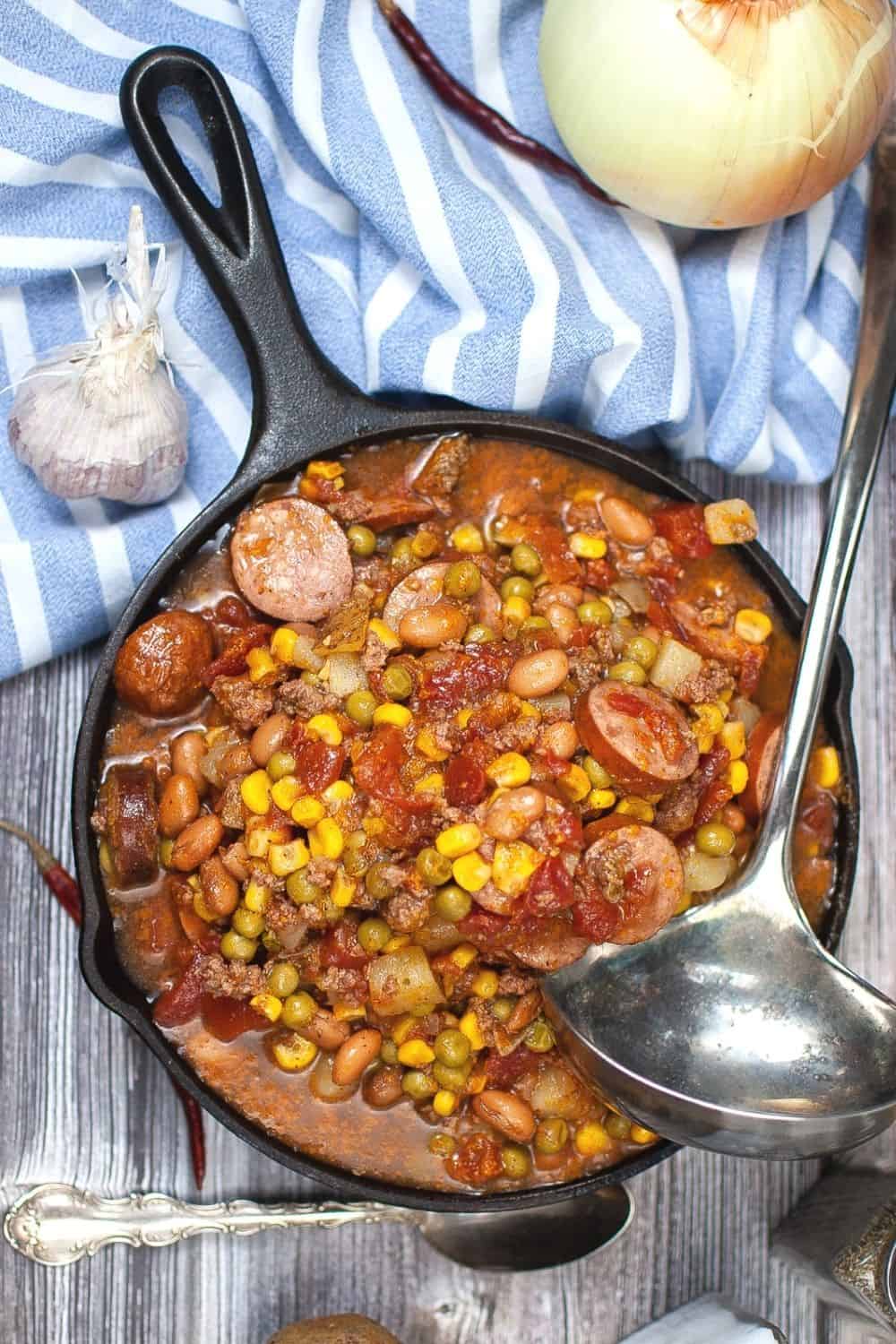 cooked cowboy stew in a cast iron skillet, next to a blue and white napkin, ready to be served.