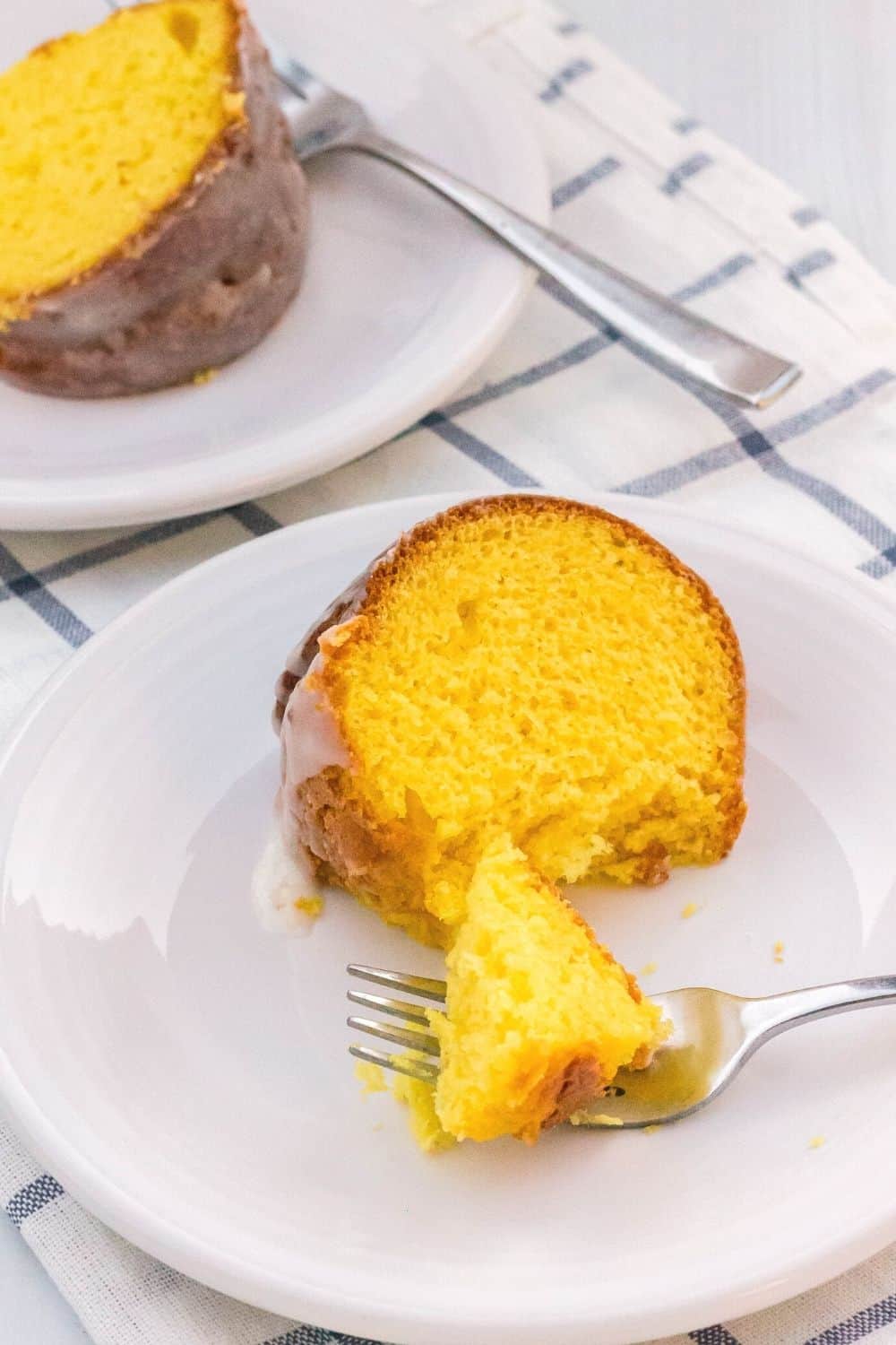 slice of lemon pudding cake on a white plate, with a bite removed with a fork.