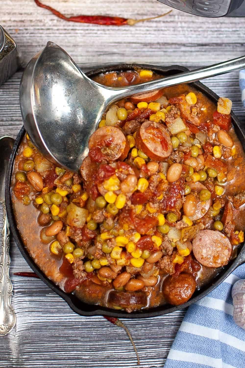 overhead view of a cast iron skillet full of cowboy stew, with a ladle resting on the dish.