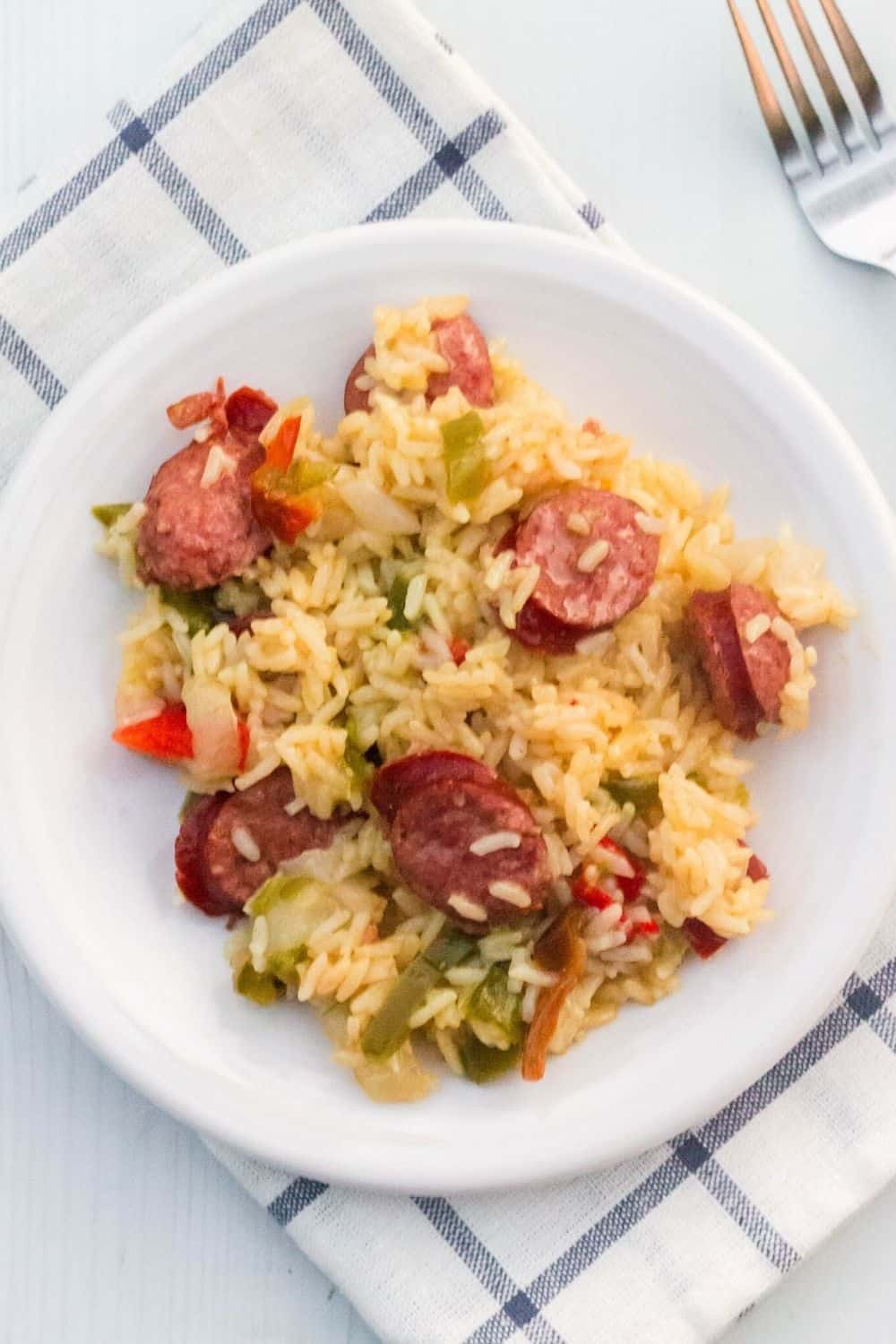 overhead view of a white plate serving sausage and rice cooked in the Instant Pot, atop a blue and white napkin