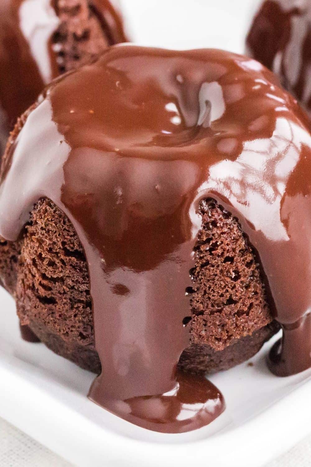 chocolate ganache drips off of a mini chocolate bundtlet, similar to Nothing Bundt Cakes, served on a white plate
