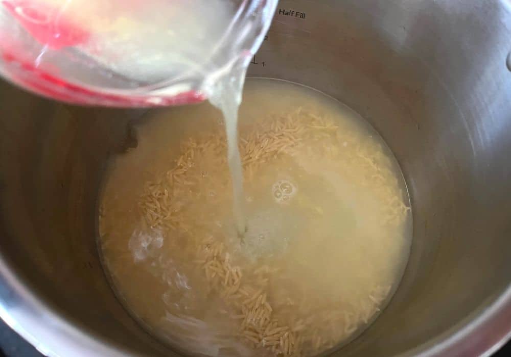chicken broth being poured over uncooked orzo into the insert pot of the Instant Pot