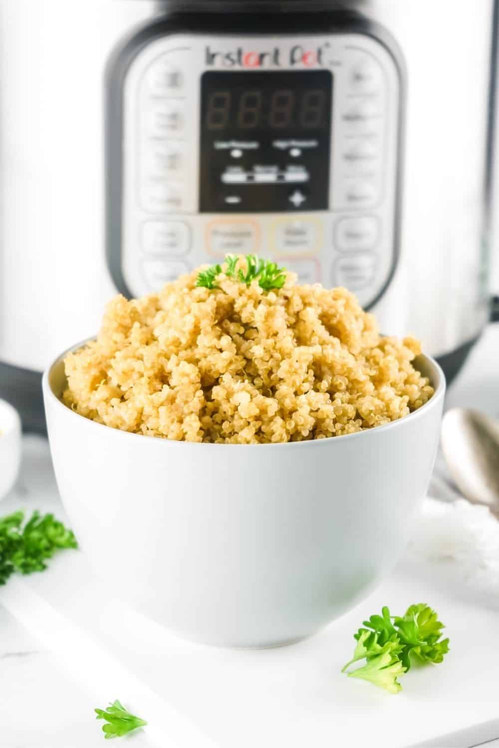 white bowl of perfectly cooked fluffy quinoa in front of an instant pot pressure cooker