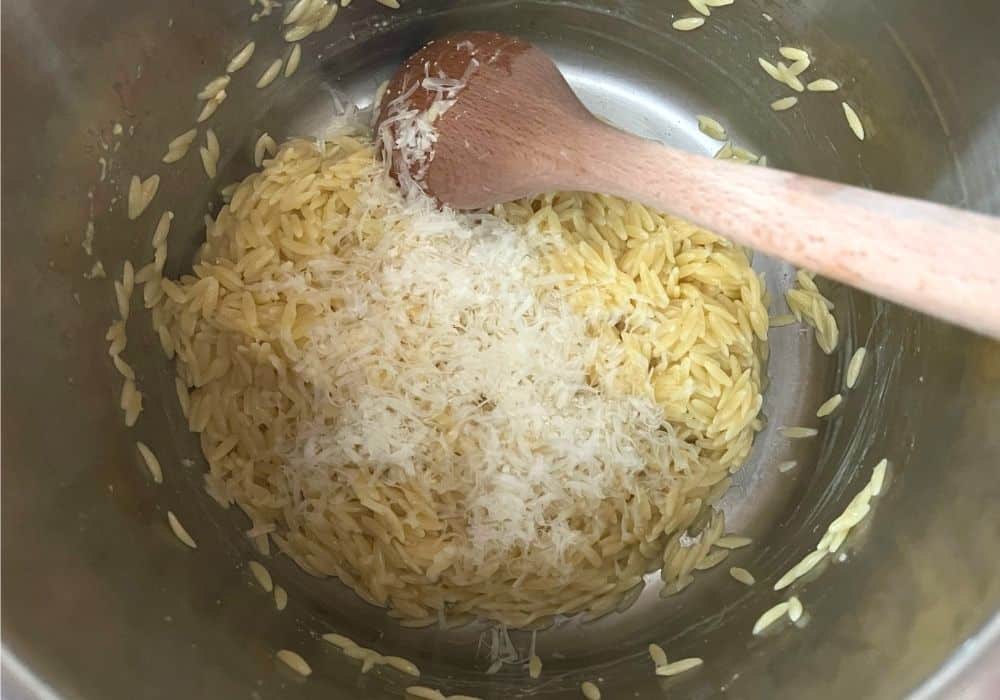 butter and grated Parmesan added to cooked orzo in the Instant Pot. A wooden spoon stirs to melt the cheese and butter.