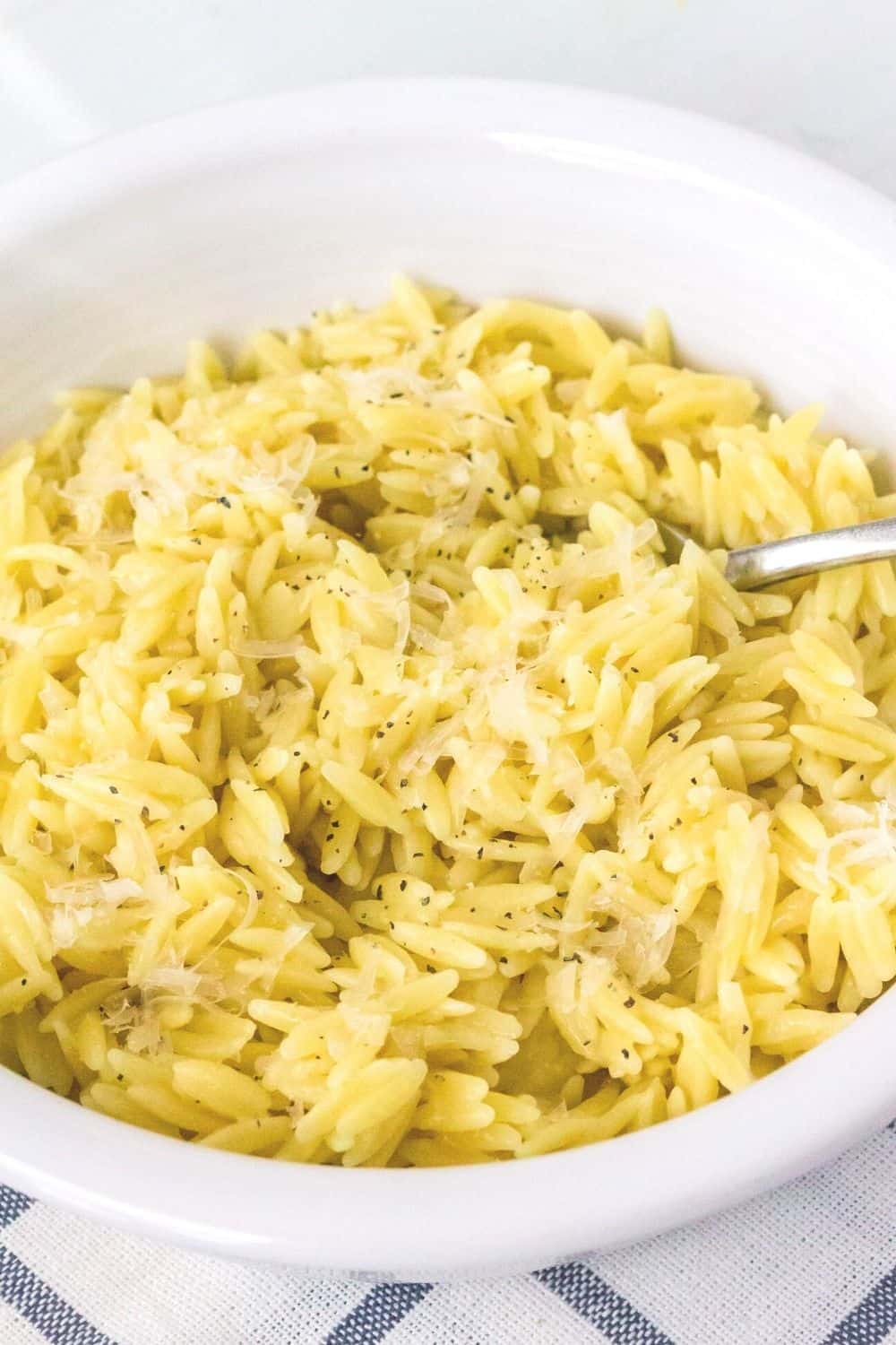 a white bowl filled with pressure cooked orzo pasta, sprinkled with salt, pepper, and grated parmesan cheese