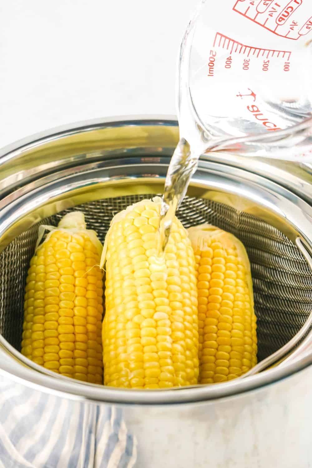water being poured over fresh corn on the cob in a steamer basket of the Instant Pot