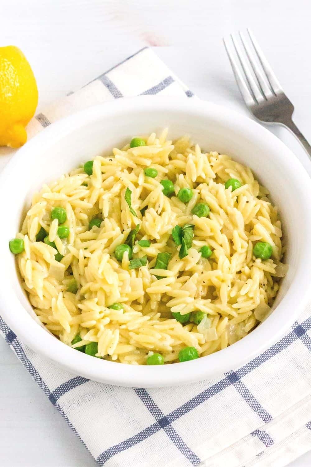 a white bowl of lemon parmesan orzo cooked in the instant pot is placed on a blue and white napkin. A lemon and fork are in the background.