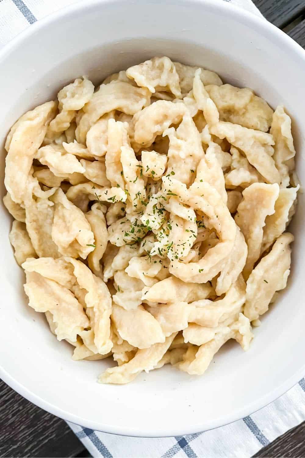 homemade German spaetzle dumplings in a white bowl, topped with parsley