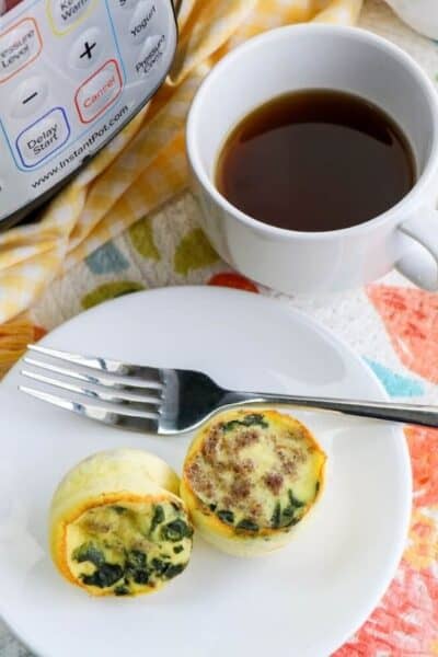 Instant Pot sausage and spinach egg bites served on a white plate in front of the pressure cooker, next to a cup of coffee