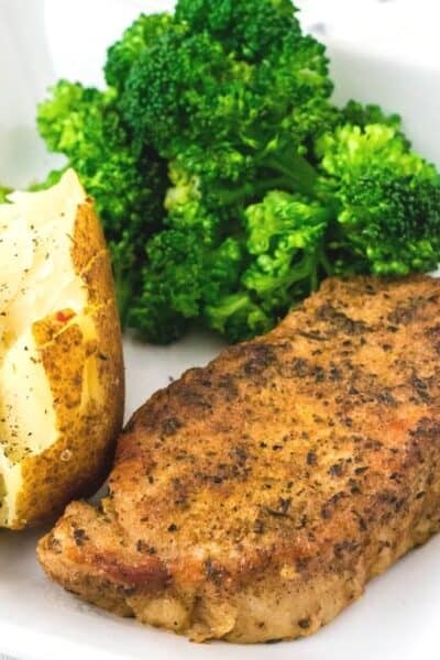 Instant Pot pork chop served on a white plate with baked potato and broccoli