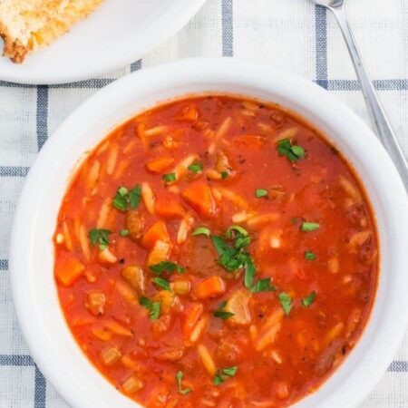white bowl of vegetable orzo soup with a plate of grilled cheese sandwiches next to it