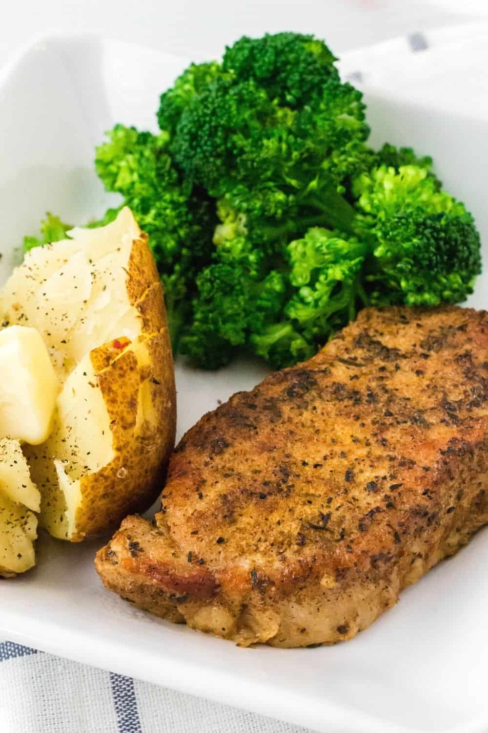 Instant Pot boneless pork chop served with baked potato and broccoli on a white plate