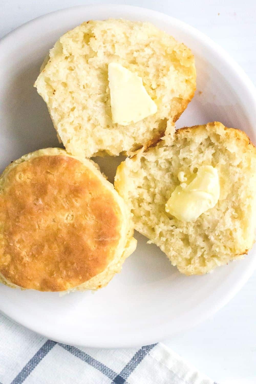 two easy homemade biscuits on a white plate, with one biscuit split open and buttered.