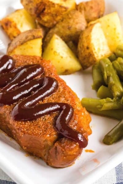 Instant Pot BBQ pork chop topped with additional sauce, served on a white plate with roasted potatoes and green beans