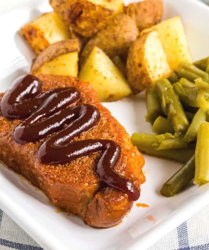 Instant Pot BBQ pork chop topped with additional sauce, served on a white plate with roasted potatoes and green beans
