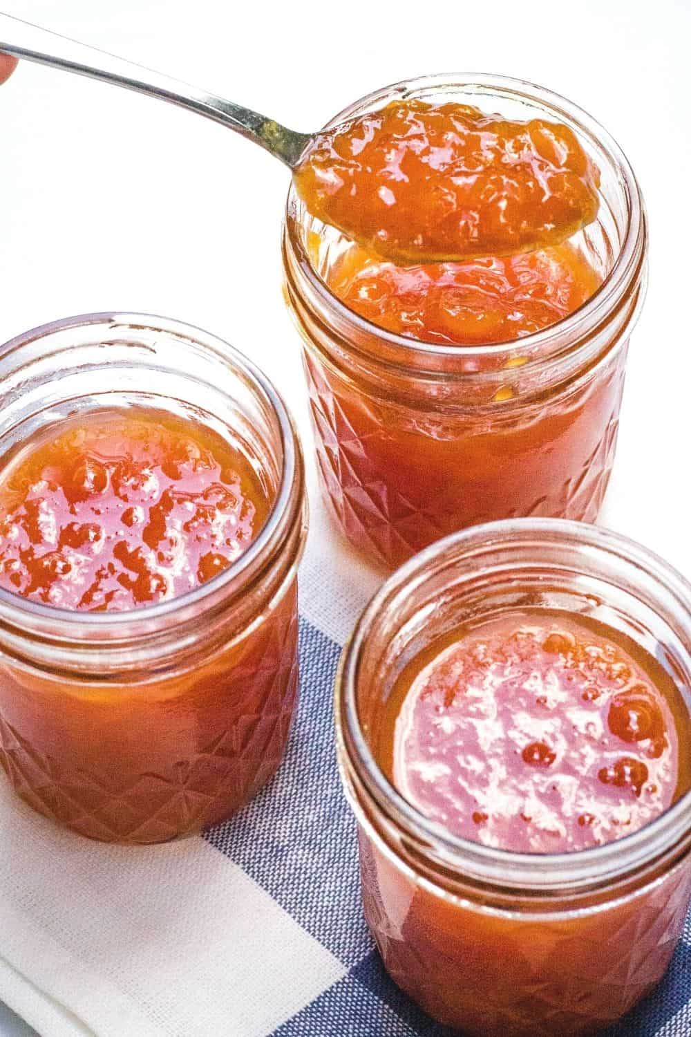 three jars of instant pot peach jam with a spoon scooping some out