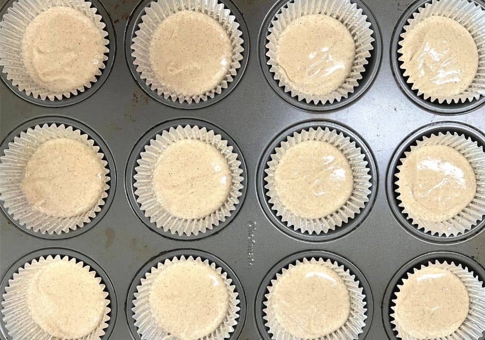 foil cupcake liners in a muffin pan, with batter filling each liner halfway.