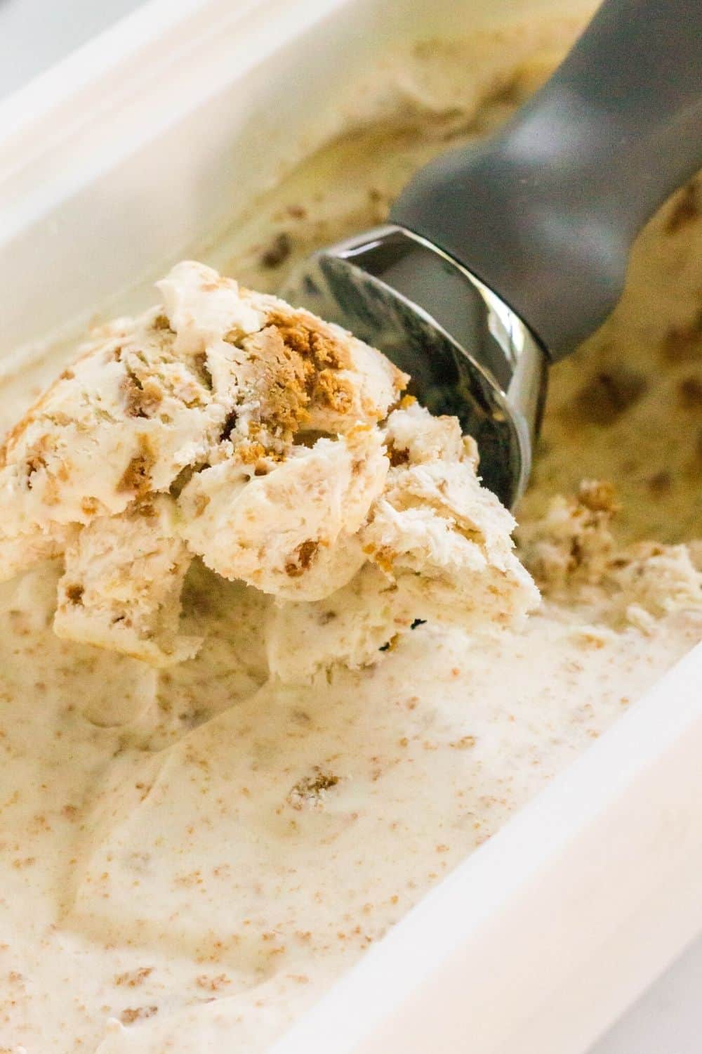 an ice cream scoop is scooping out some homemade lotus biscoff ice cream from its freezer container.