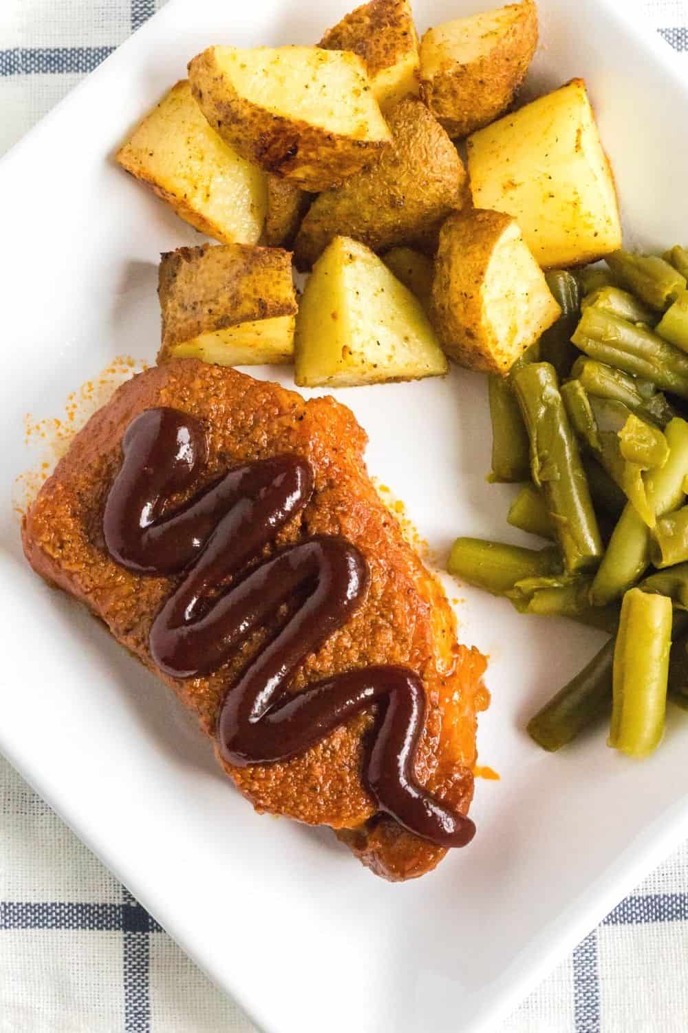 overhead view of a white plate with a pressure cooker boneless bbq pork chop, green beans, and roasted potatoes