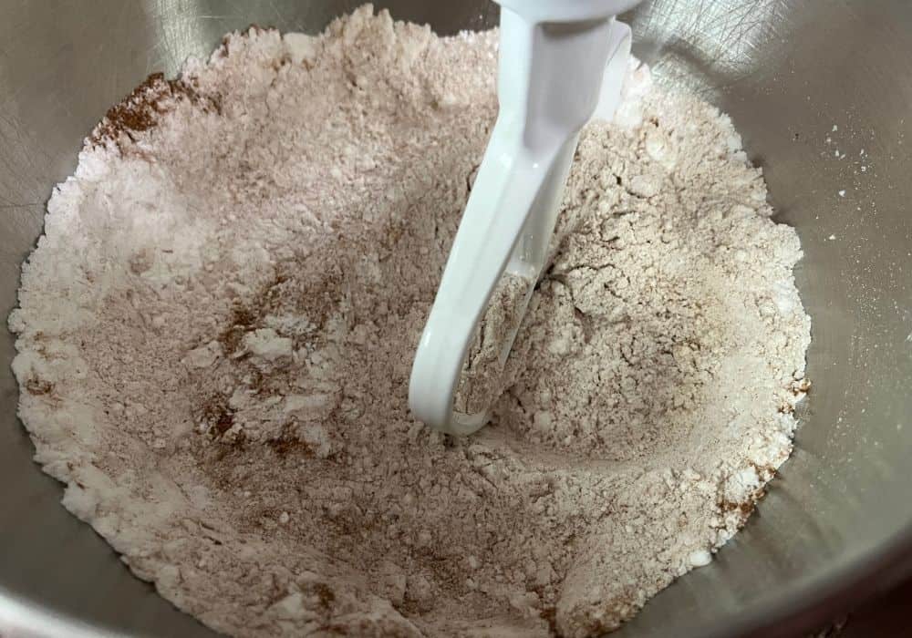 cake mix, pudding mix, and cinnamon being mixed together in the bowl of a stand mixer