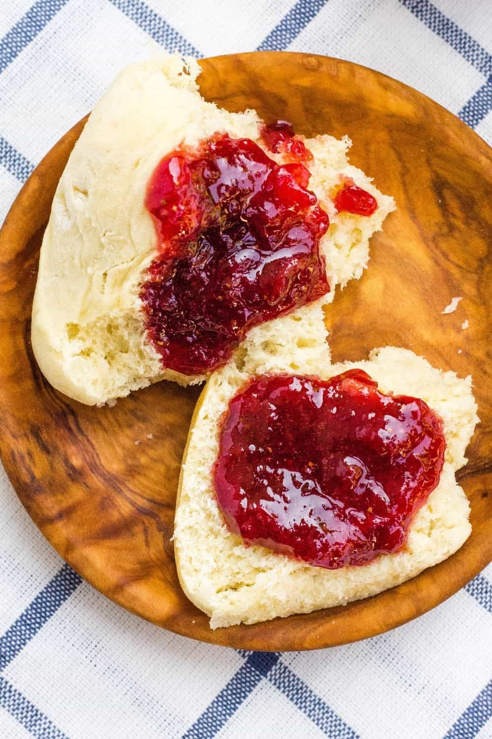 instant pot strawberry jam spread on two dinner rolls atop a wooden plate