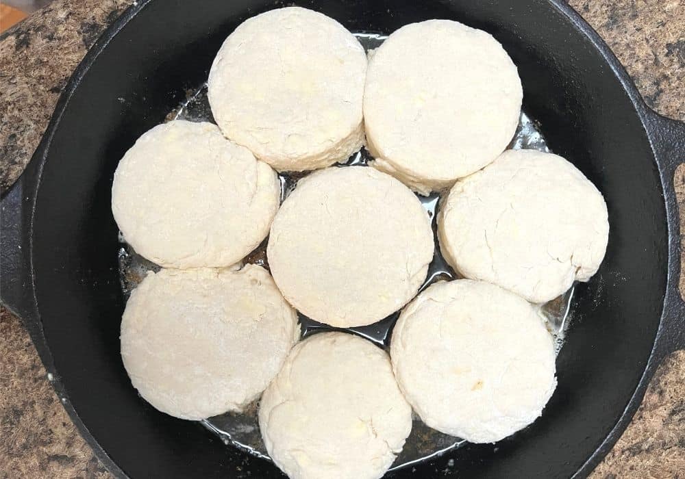 eight rounds of unbaked homemade biscuits in melted butter in a cast iron pan, ready for baking