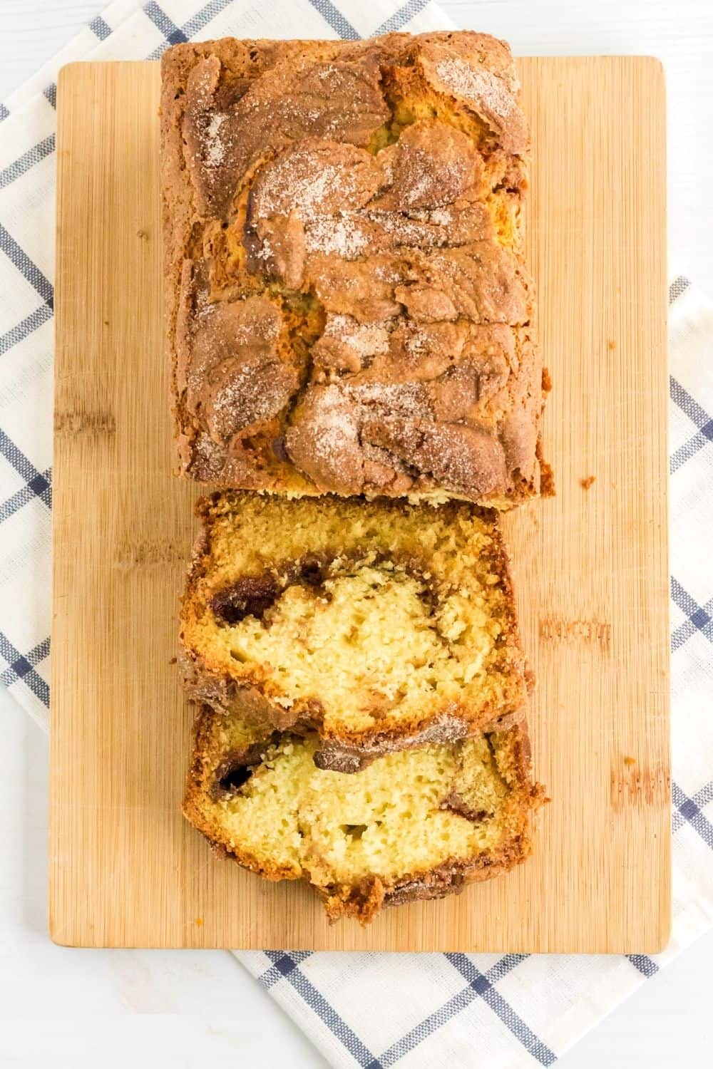 overhead view of a partially sliced loaf of Amish cinnamon bread on a cutting board, atop a blue and white napkin