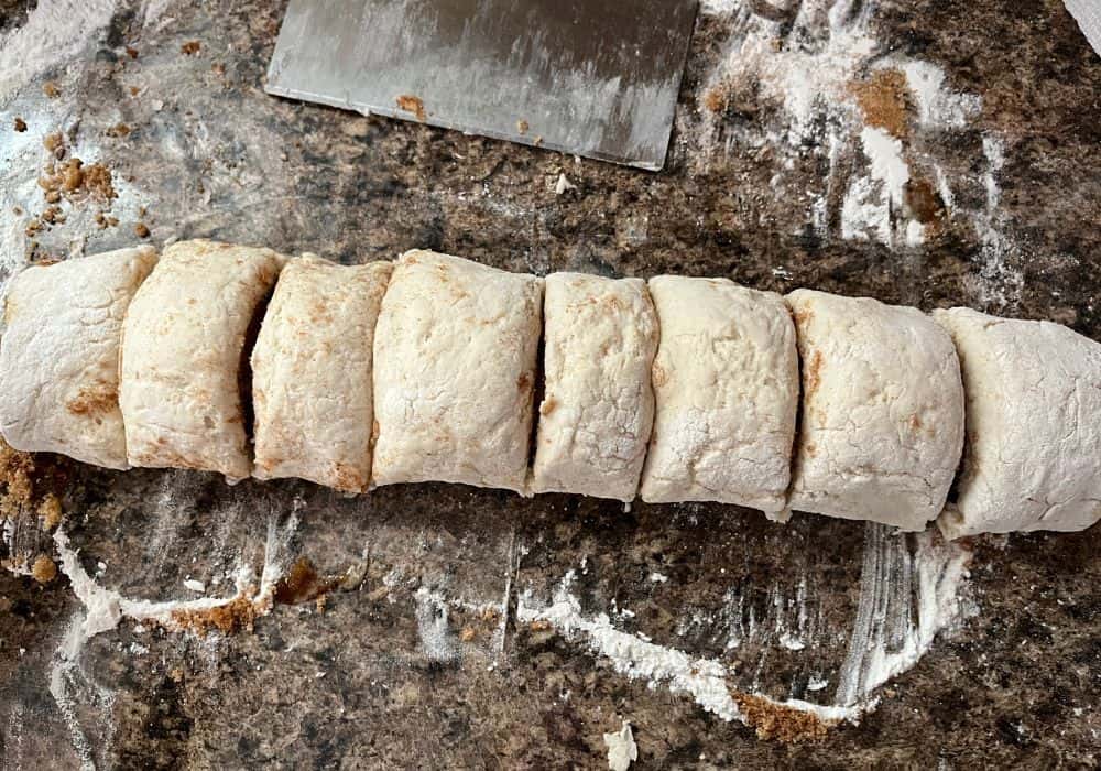 cinnamon roll dough rolled up into a log and cut into eight pieces