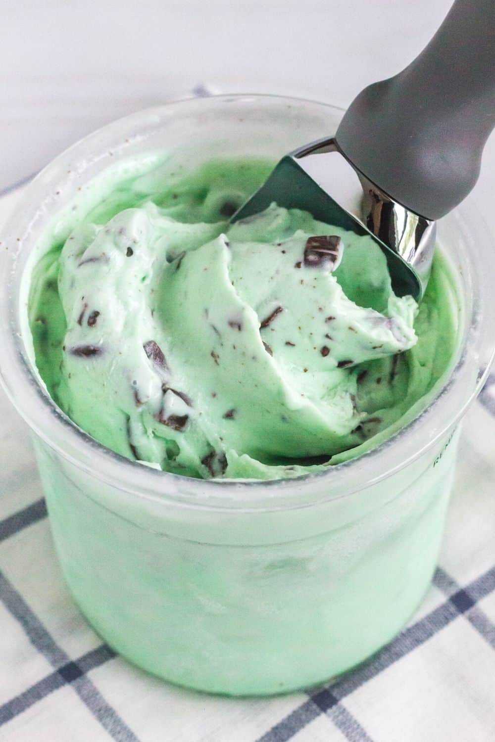 an ice cream scoop rests in a pint of mint chocolate chip ice cream made in the Ninja Creami machine.