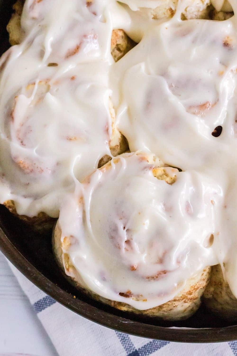 cream cheese frosting spread over cinnamon rolls in the pan