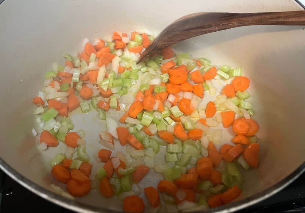 onions, carrots, and celery being sauteed in a dutch oven, with a wooden spatula.