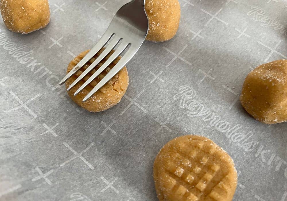 the tines of a fork pressing a cross hatch pattern into peanut butter cookie dough