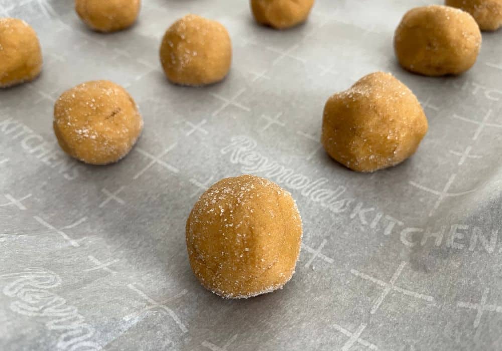 peanut butter cookie dough balls rolled inn sugar and placed on a parchment lined baking sheet